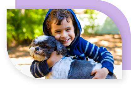 A young boy holding a black and white dog and smiling.