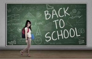 A student standing in front of a chalkboard that says Back to school in large chalked letters