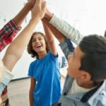 Kids in a circle with one arm in the air bring all their hands together in the middle.