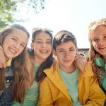 Four pre-teens lined up with arms around each other and smiling.
