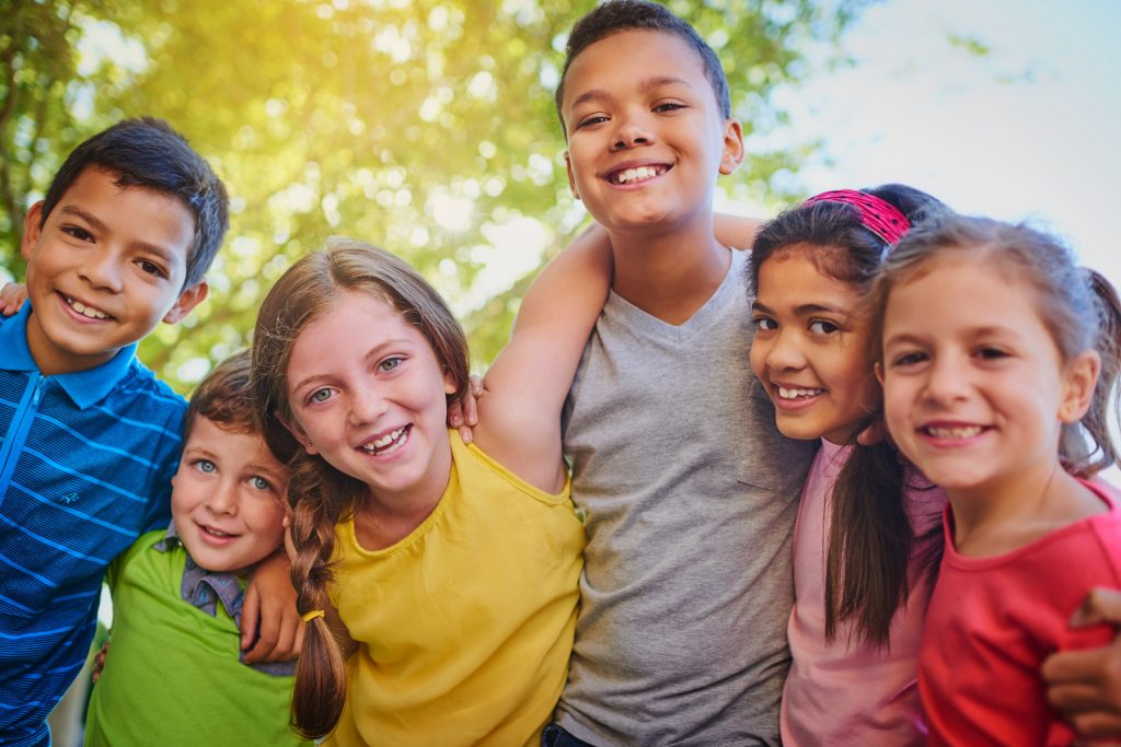 Six young children with their arms around each other, looking at the camera and smiling.