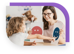 A child pointing at a smiley face that is being held up by a therapist. The therapist has a sad face in her other hand.